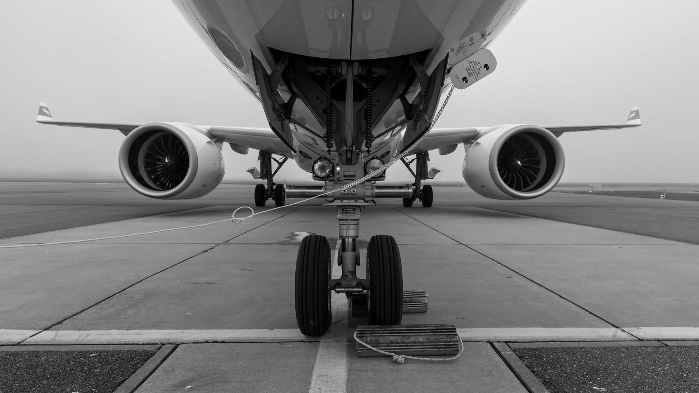 An airliner head on in fog, nose gear and both engines square to the camera, photographed in black and white.