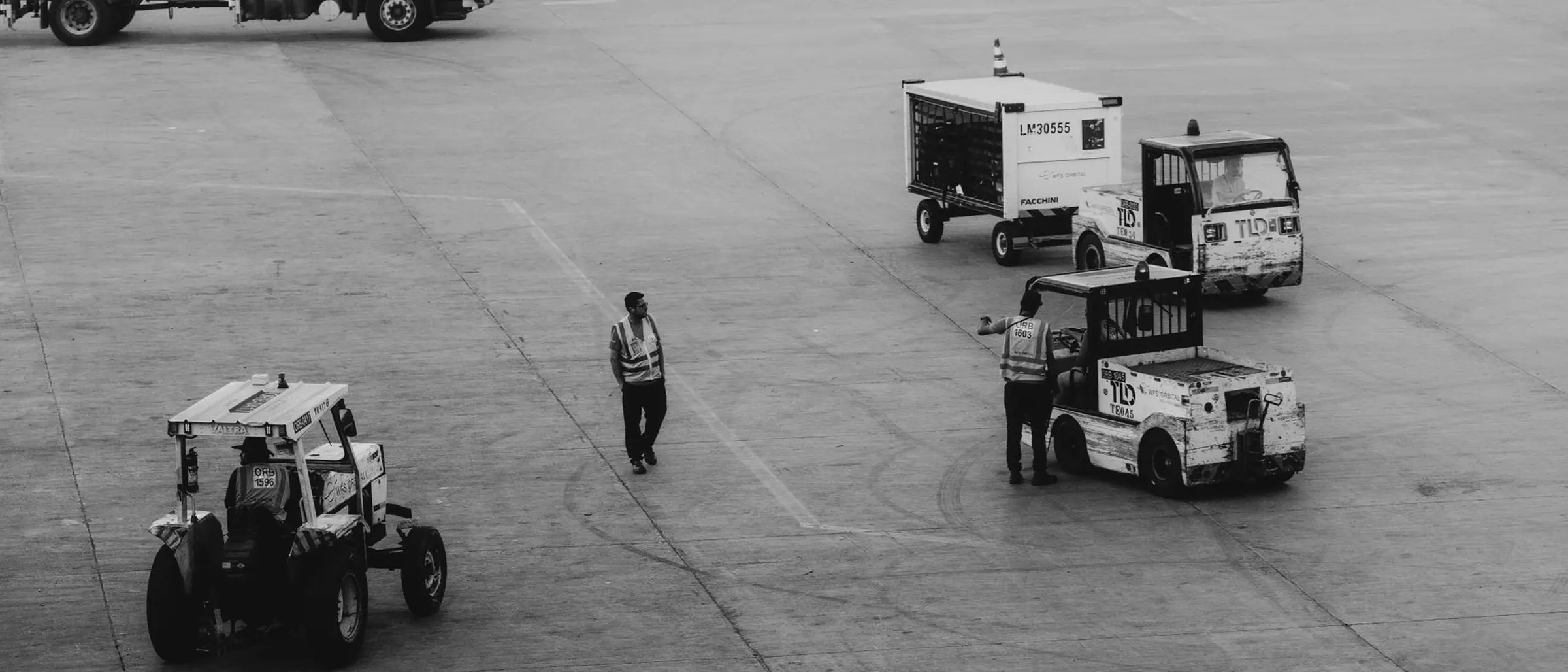Airport ground crew at work across an apron, photographed in black and white.