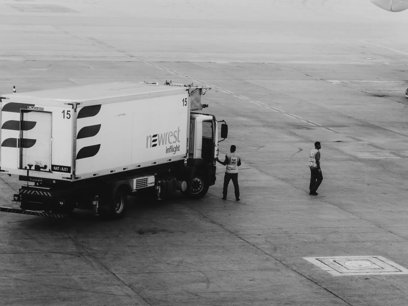 Ground support vehicles and crew working an airport apron, photographed in black and white.